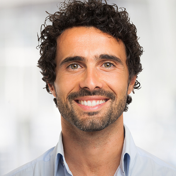 A smiling man with dark hair, wearing a blue shirt, against a white background.