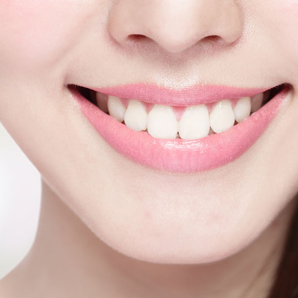 The image shows a close-up of a person smiling with straight white teeth, displaying a wide smile with pink lipstick.