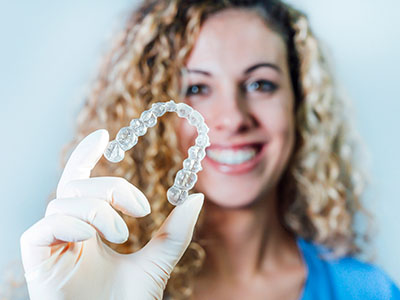 A woman holding up a transparent dental retainer with her left hand against a white background.