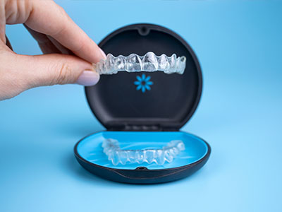 The image shows a person s hand holding an open case containing a set of clear aligners, which are used for teeth straightening.