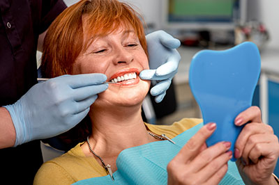 A woman with red hair sitting in a dental chair, receiving dental care from a professional, holding up a blue dental model for examination.