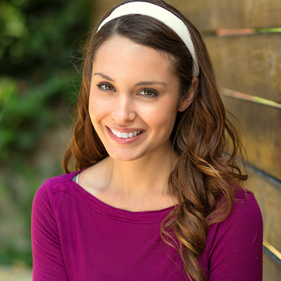 Woman with long hair wearing a pink top and a white headband, smiling and posing for a portrait.