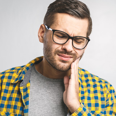 A man with glasses and a beard, wearing a yellow plaid shirt, is looking upwards with his hand on his chin, possibly in contemplation or decision-making.