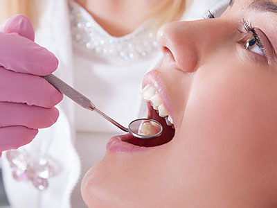 An image depicts a dental professional performing oral care on a patient s teeth, with the patient seated and wearing a pink surgical gown and a mouthpiece with an attached suction device.