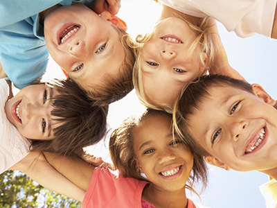 A group of children posing together with smiles on their faces under a clear sky.