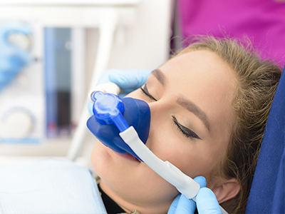 A person receiving medical treatment with a blue oxygen mask attached to their face, being attended to by a healthcare professional.
