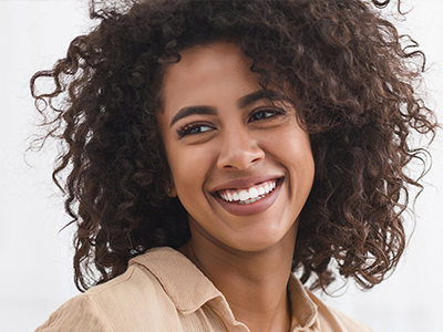 The image shows a smiling woman with curly hair, wearing a light-colored top, against a plain background.