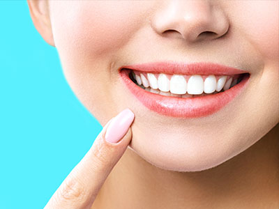 The image shows a close-up of a person s face with a bright smile, focusing on their teeth and lips against a light blue background.